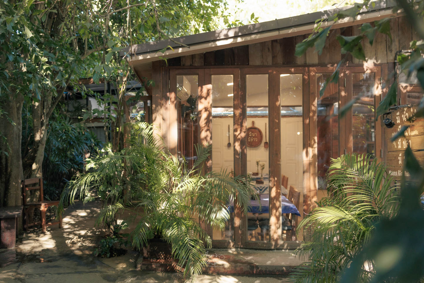 清邁 Meena 餐廳隱匿在茂密綠色植物後的木造玻璃小屋，透過大片落地玻璃窗能看見溫馨舒適的室內用餐區｜by Ann's Little Space