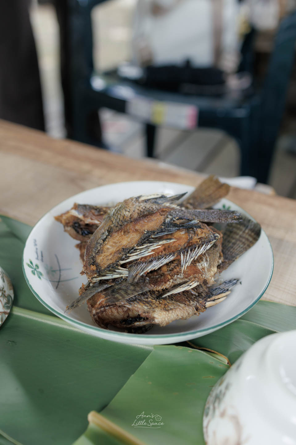 一盤剛炸好、色澤金黃的酥脆魚肉料理，置於鋪著月桃葉的餐桌上。｜by Ann's Little Space